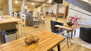 A spacious loft-style living area with high ceilings, exposed beams, and a mix of seating options including a sofa, chairs, and a dining table. - The Carriage House - Downtown (Chillicothe)