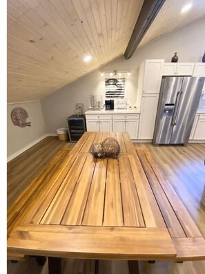 Une cuisine avec une table en bois, des placards blancs et un réfrigérateur en acier inoxydable.