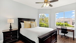 A bedroom with a bed, a desk, a chair, a nightstand, and a ceiling fan.