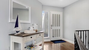 A hallway with a white console table, a mirror, a sailboat decoration, and a door leading to another room.