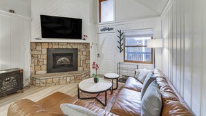 A living room with a stone fireplace, leather sofa, and a flat-screen TV mounted above the fireplace. - Centrally Located Angel Fire Condo ~ 1/2 Mi Resort (Angel Fire)