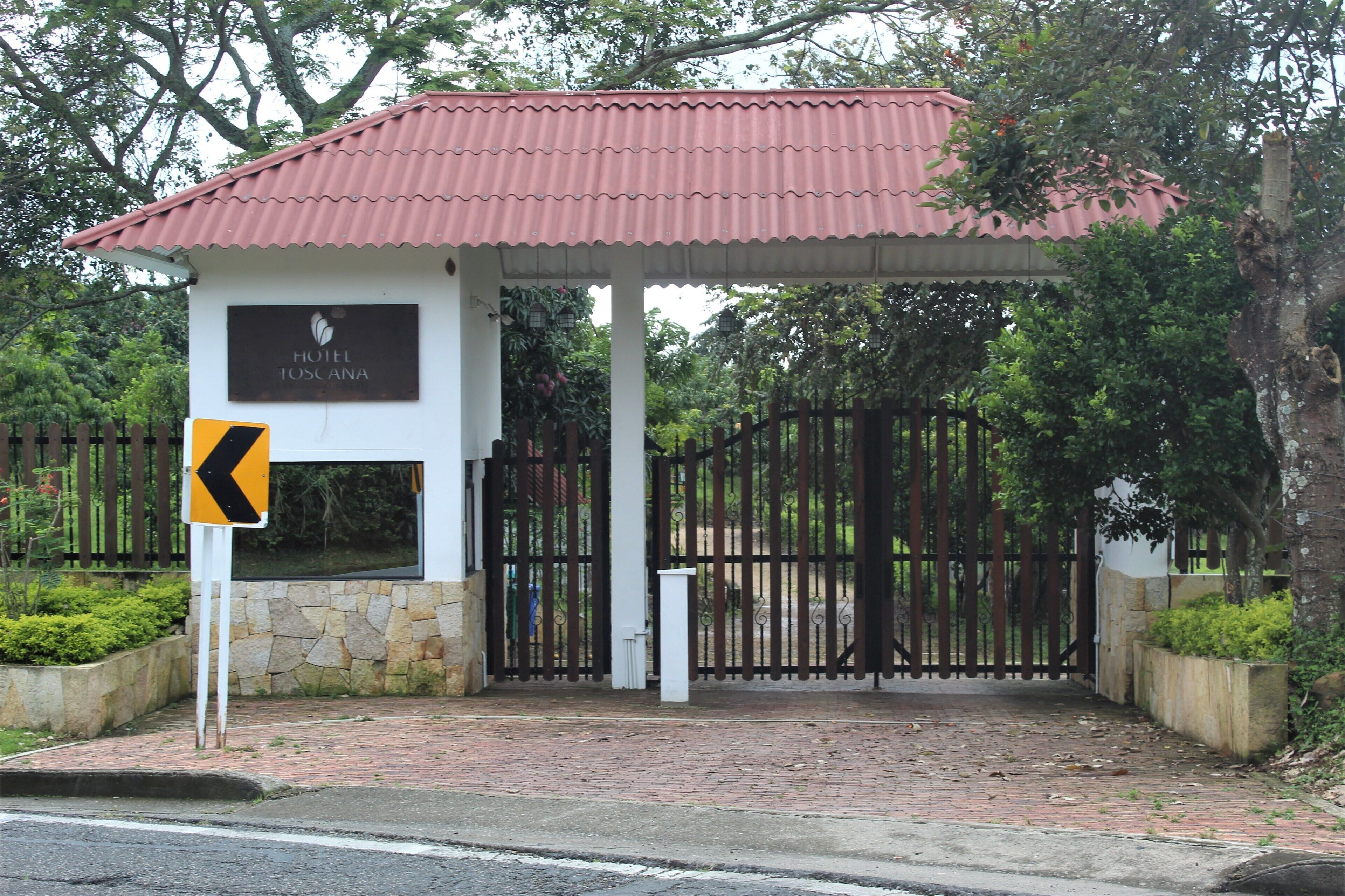 A hotel entrance with a red roof, a stone wall, and a gated driveway.