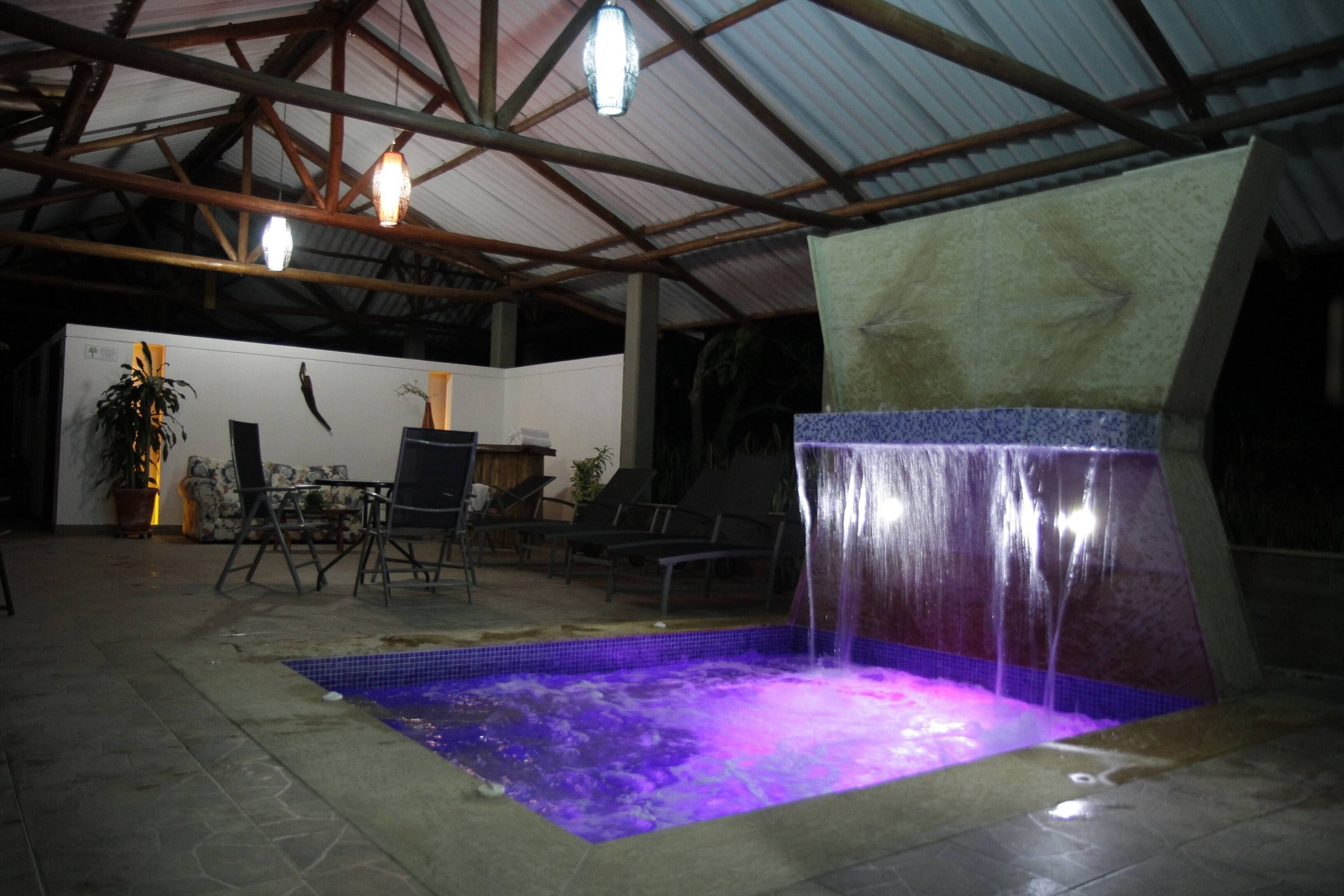 Une piscine intérieure agrémentée d’une cascade, entourée de chaises longues et d’une plante en pot.