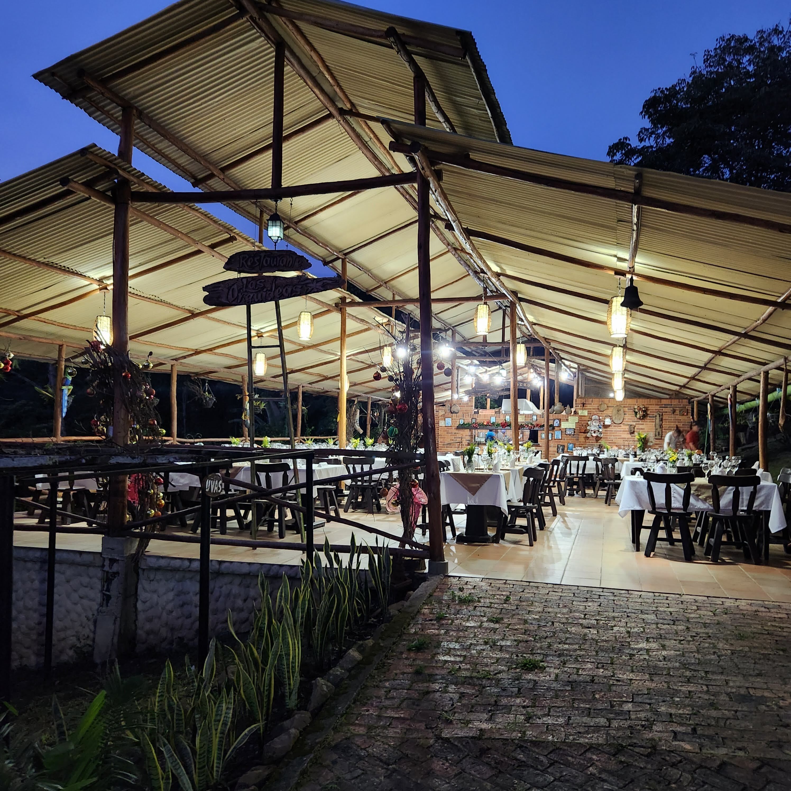Un espacio de comedor al aire libre con mesas y sillas bajo una estructura cubierta.