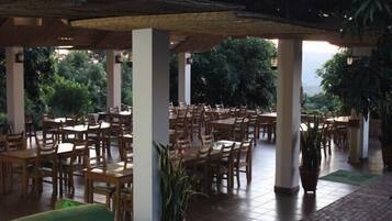An outdoor dining area with wooden tables and chairs, potted plants, and a covered section with columns.
