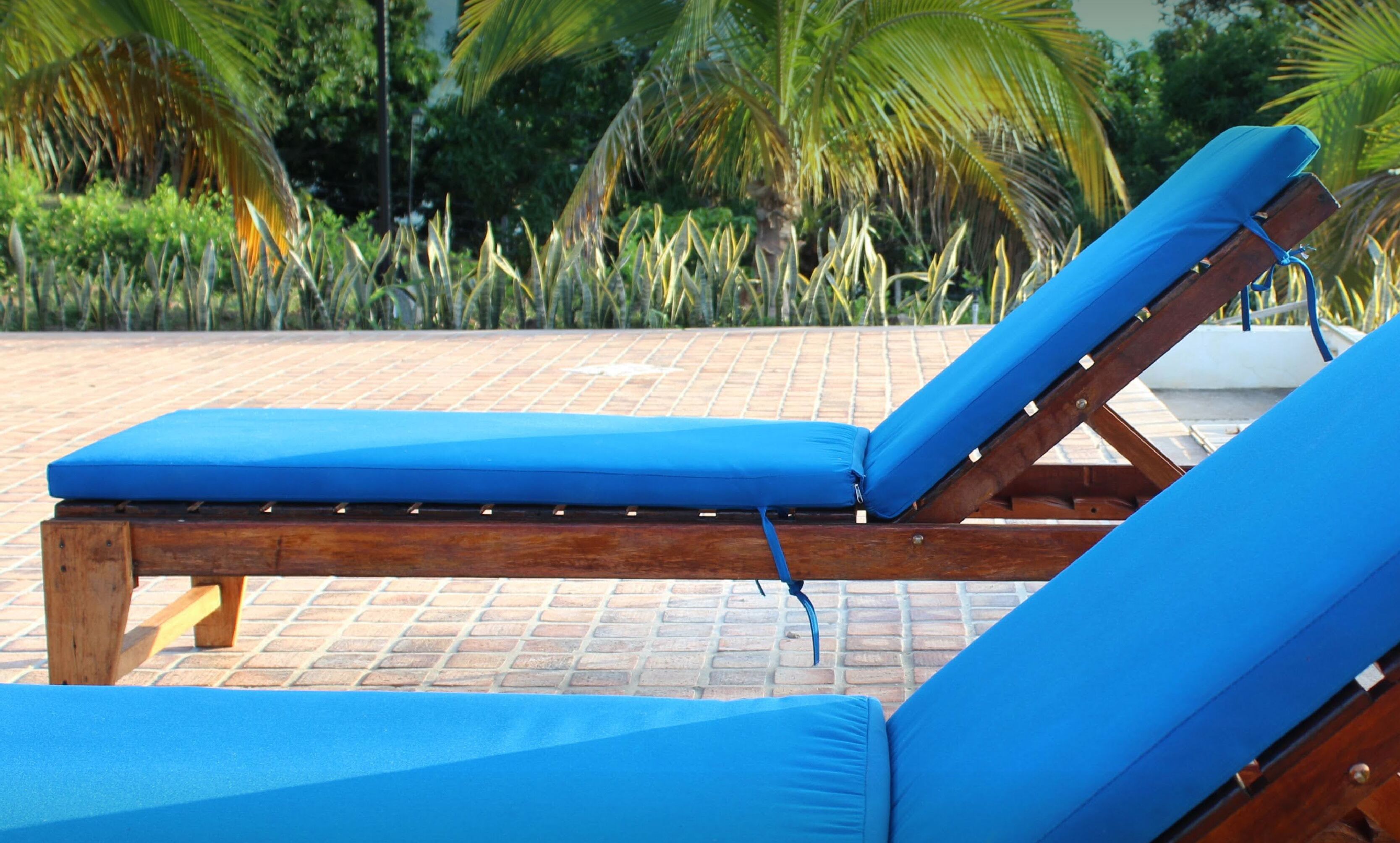 Una silla de lounge de madera con un cojín azul, ubicada en un patio con suelo de baldosas y diseño de ladrillo.