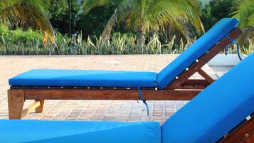 Una silla de lounge de madera con un cojín azul, ubicada en un patio con suelo de baldosas y diseño de ladrillo.