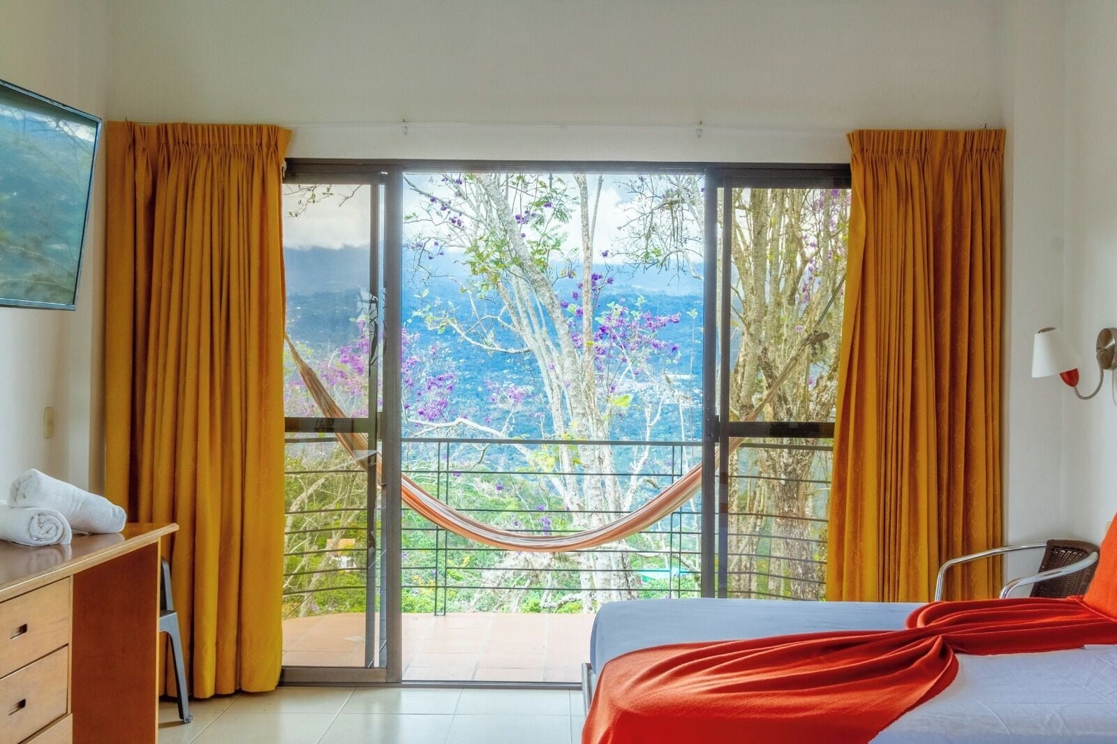 Una habitación con cama, escritorio y ventana con cortinas.