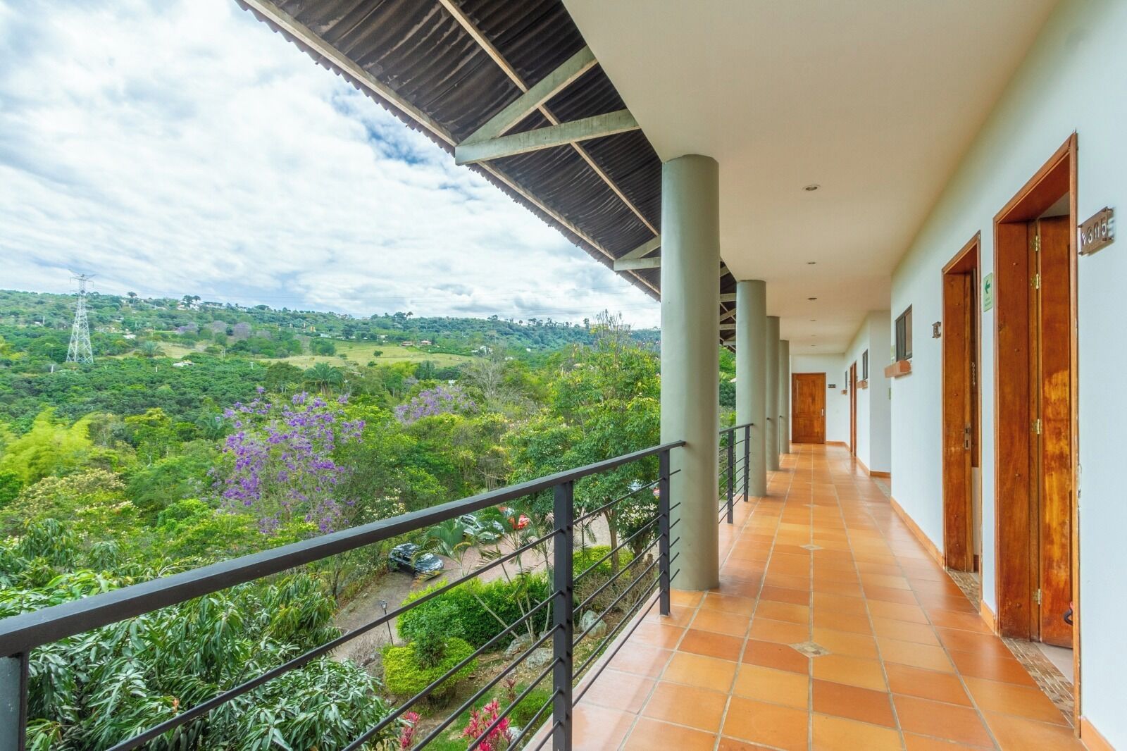 Un pasillo con vistas a un paisaje exuberante, piso de baldosas y un balcón con barandilla.