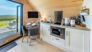 A modern kitchen with a large window, a flat-screen TV, and a dining area with a table and chairs. - 1 bedroom accommodation in Talybont, near Borth (Talybont, near Borth)