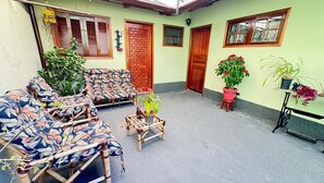 Ein überdachter Außenbereich zum Sitzen mit einer Couch, Sesseln, einem kleinen Tisch und Kübelpflanzen.