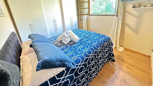 Ein Schlafzimmer mit Bett, Kissen, einem Schrank und einem Fenster mit Blick ins Grüne.