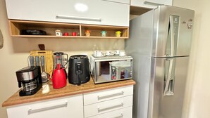 Eine kompakte Küchenzeile mit Edelstahlkühlschrank, Kaffeemaschine, Mixer und Toaster auf einer Holzarbeitsfläche.