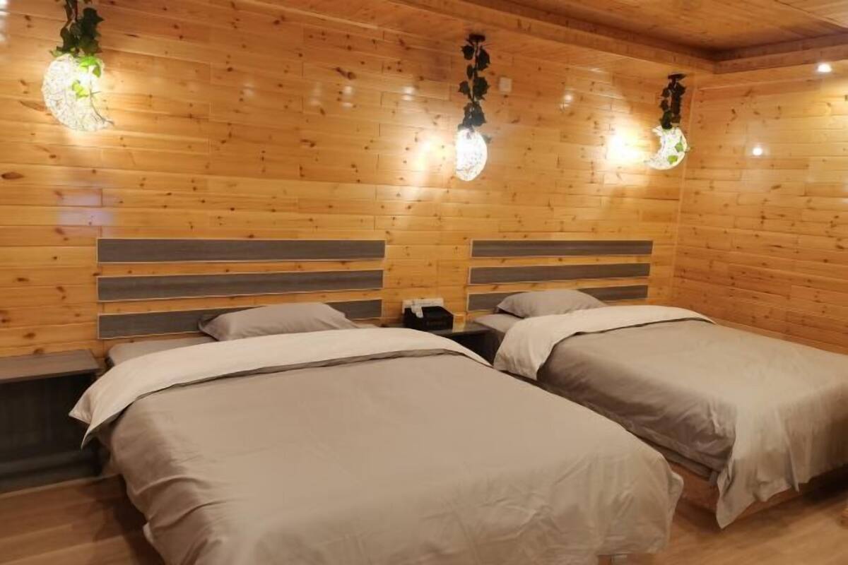 A room with two beds, wooden walls, and hanging lights.
