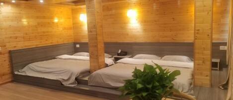 A wooden cabin-style room with two beds, a small table with a plant, and a wooden cabinet.