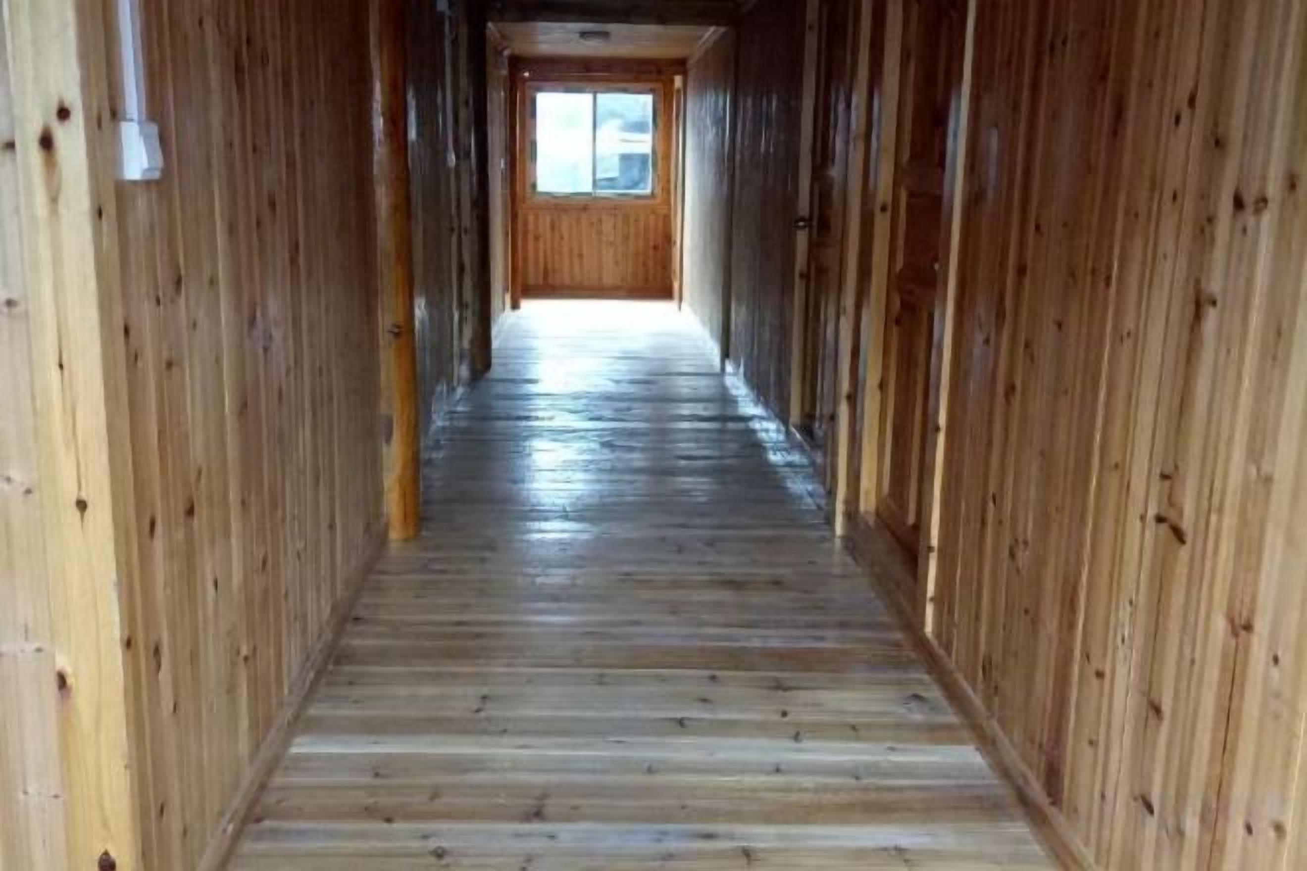 A wooden hallway with a wooden floor and walls, leading to a door at the end.