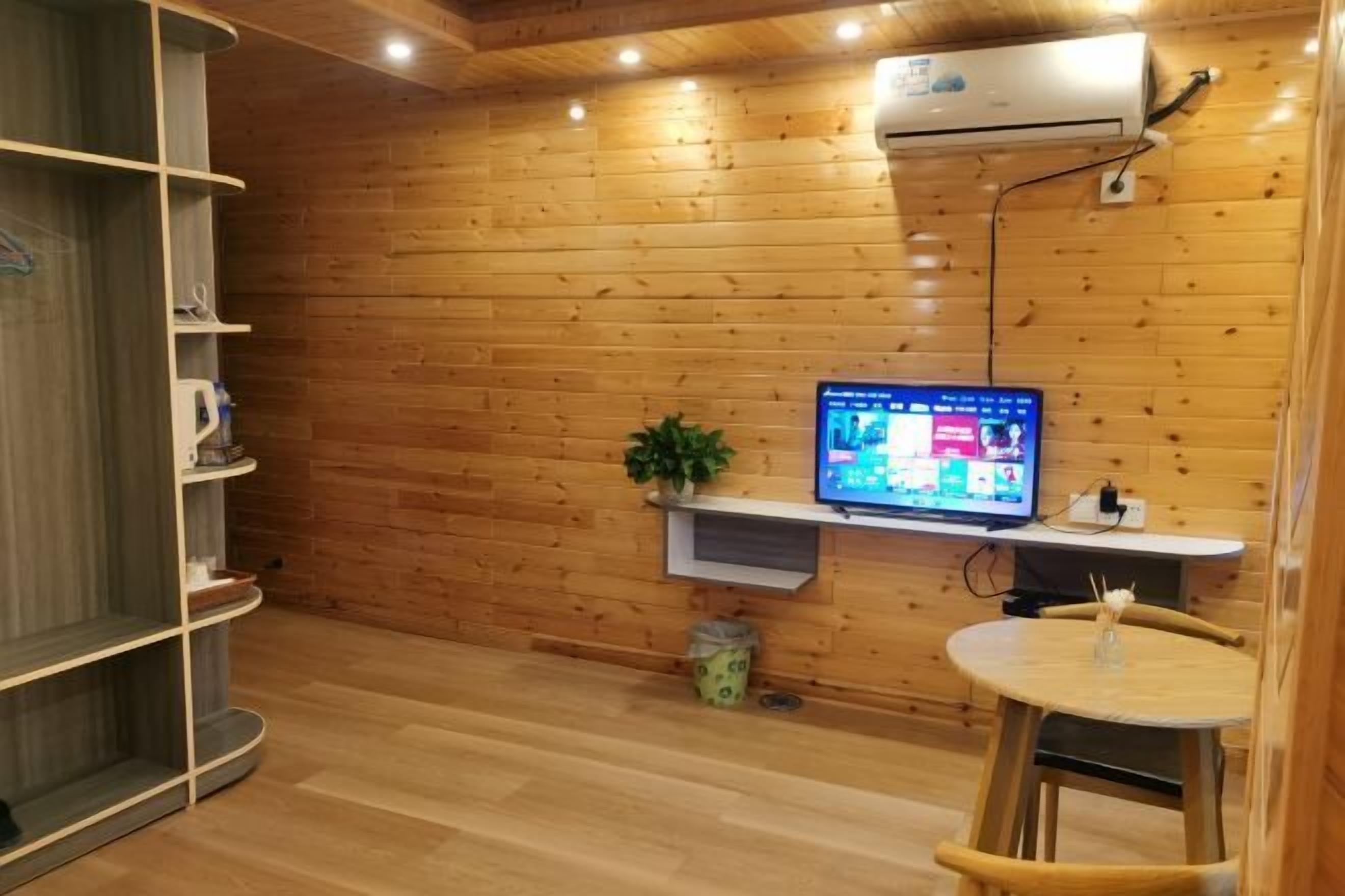 Ein Zimmer mit Holzwänden, einem Wand-Fernseher, einem kleinen Tisch mit Stuhl und einem Regal.