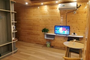 A room with wooden walls, a mounted TV, a small table with a chair, and a shelf unit. - Sanjiang Qingtian Yuese Homestay (Sanjiang)