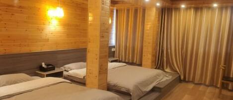 A wooden cabin-style room with three beds, a small table, and a curtain.