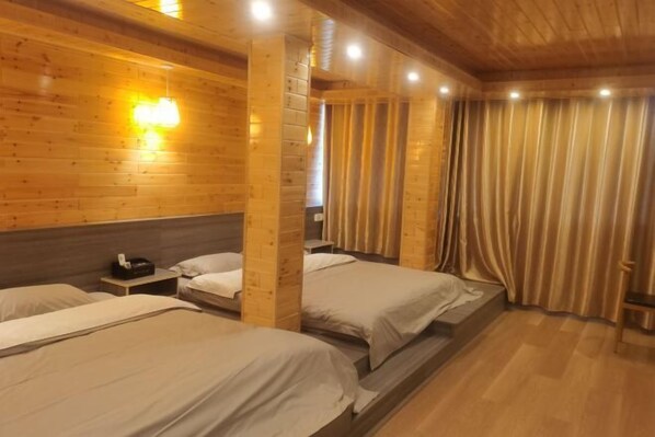 A wooden cabin-style room with three beds, a small table, and a curtain.