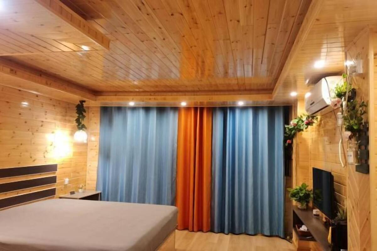 A wooden-paneled room with a bed, curtains, a TV, and wall-mounted plants.