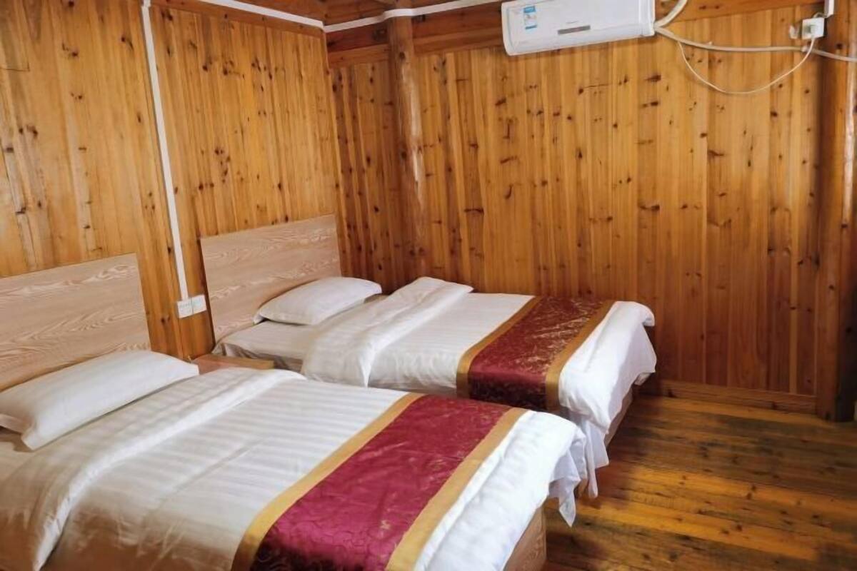 A wooden-paneled room with two beds, each with white bedding and a red and gold bedspread.