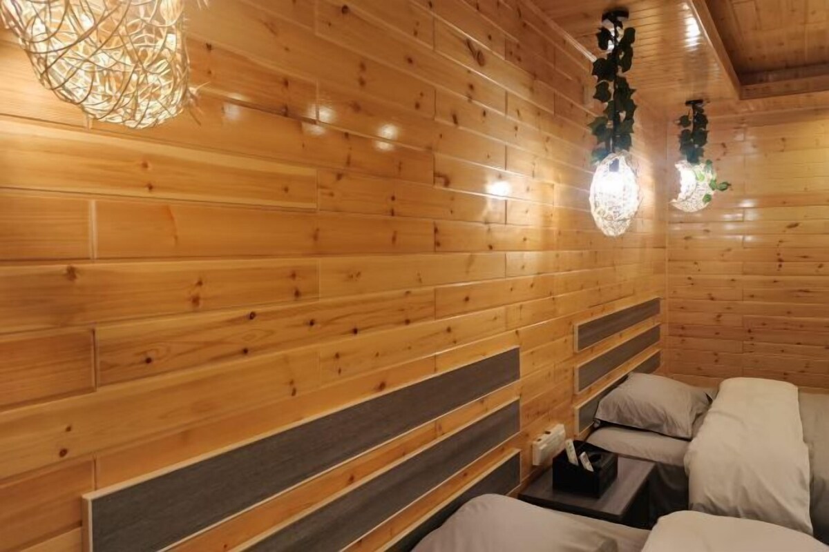 A wooden cabin interior with a bed, a small table, and a hanging light fixture.