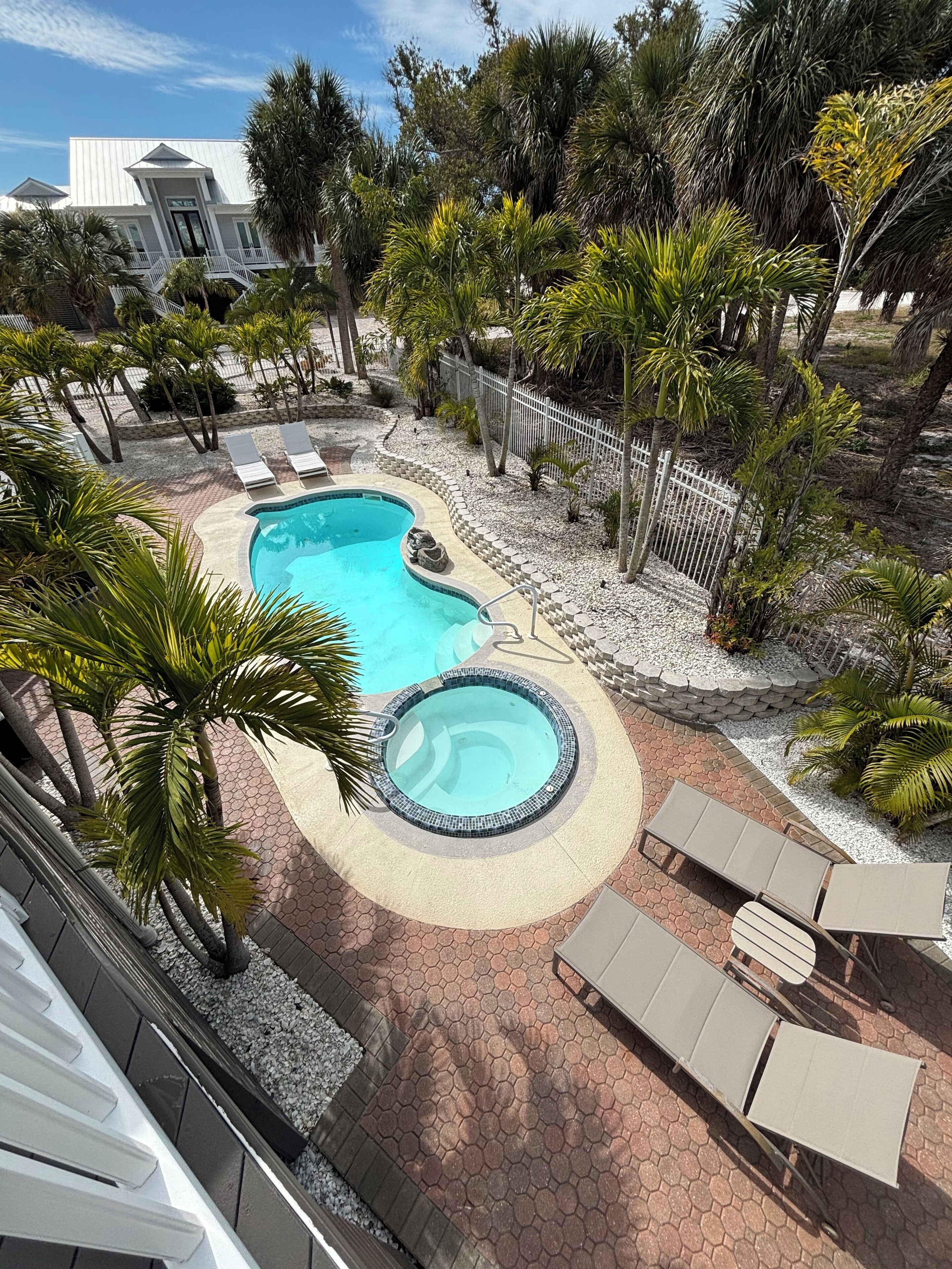 Une piscine avec un jacuzzi, entourée de palmiers et de chaises longues.