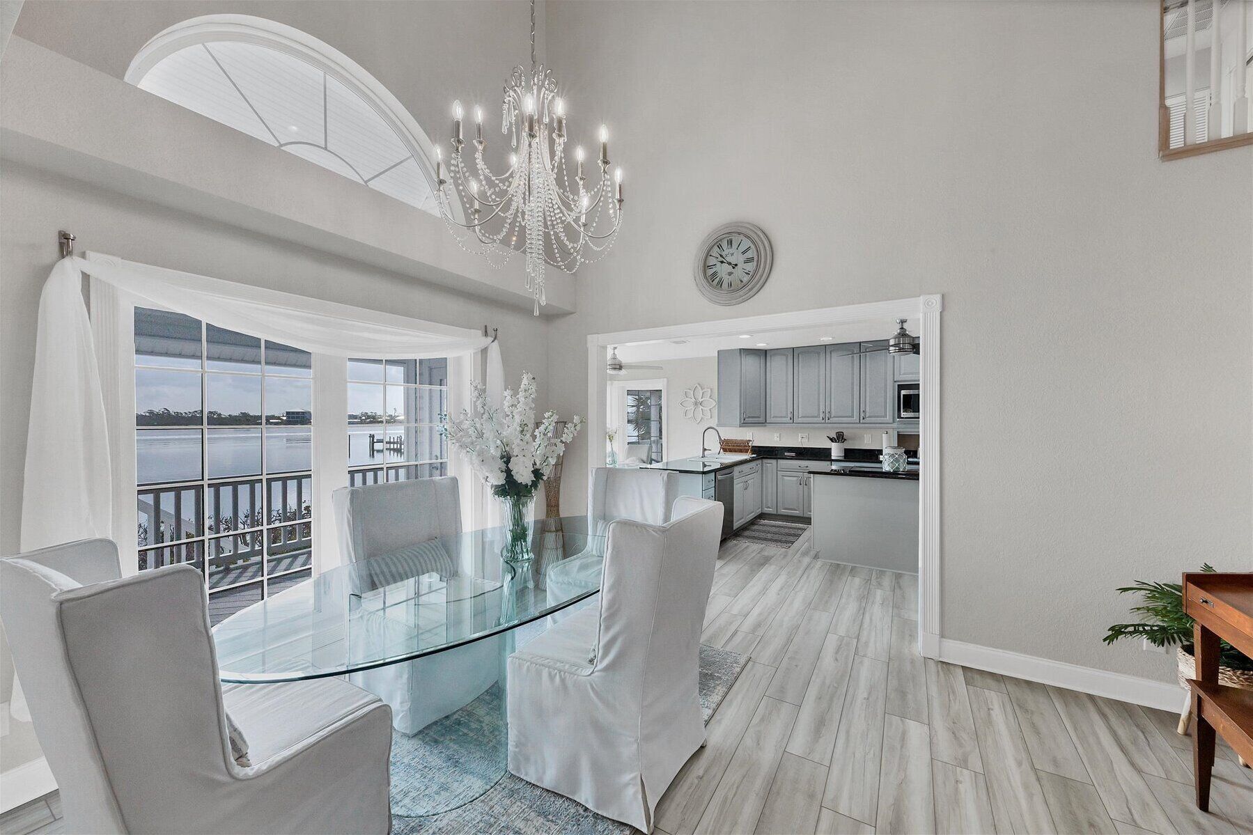A modern kitchen with grey cabinets, a central island, and a dining area with a glass table and chairs.