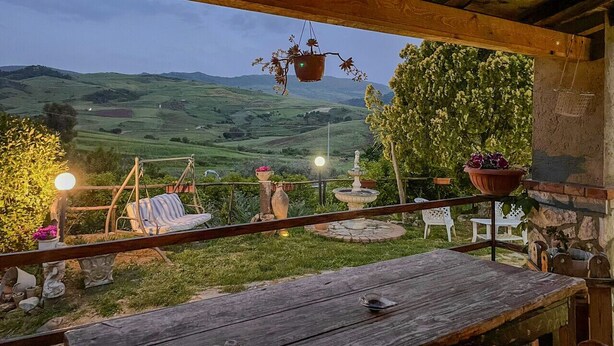 Un terrazzo in legno con una sedia a dondolo, un tavolo e un vaso sospeso.