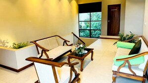 A spacious living area with a sofa, armchairs, and a coffee table. A large window offers a view of greenery outside. - Rivorich Residence Kandy (Sirimalwatta)