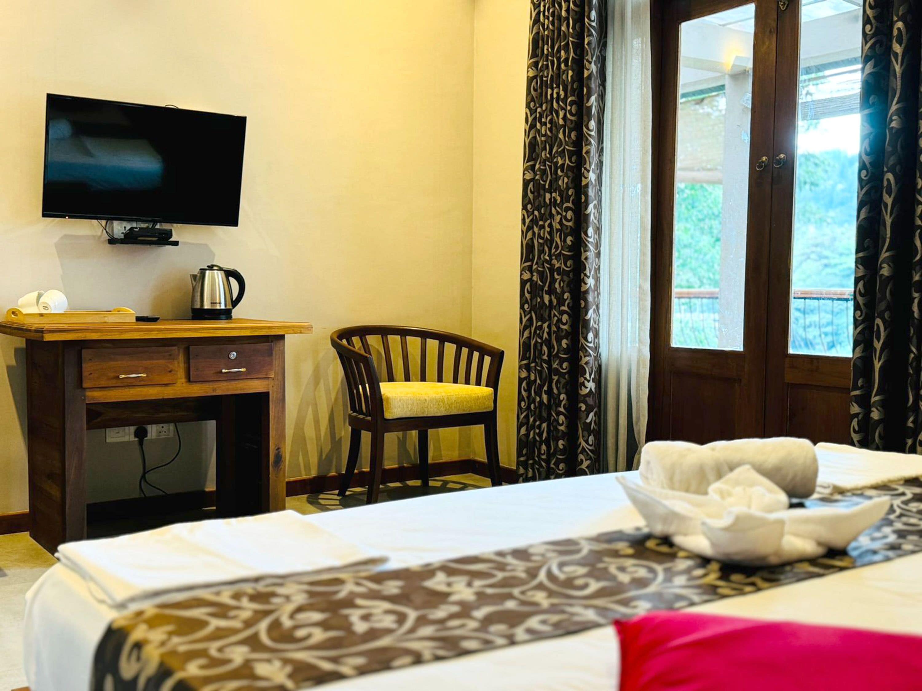 A hotel room with a bed, a desk with a television, a chair, and a window with curtains.