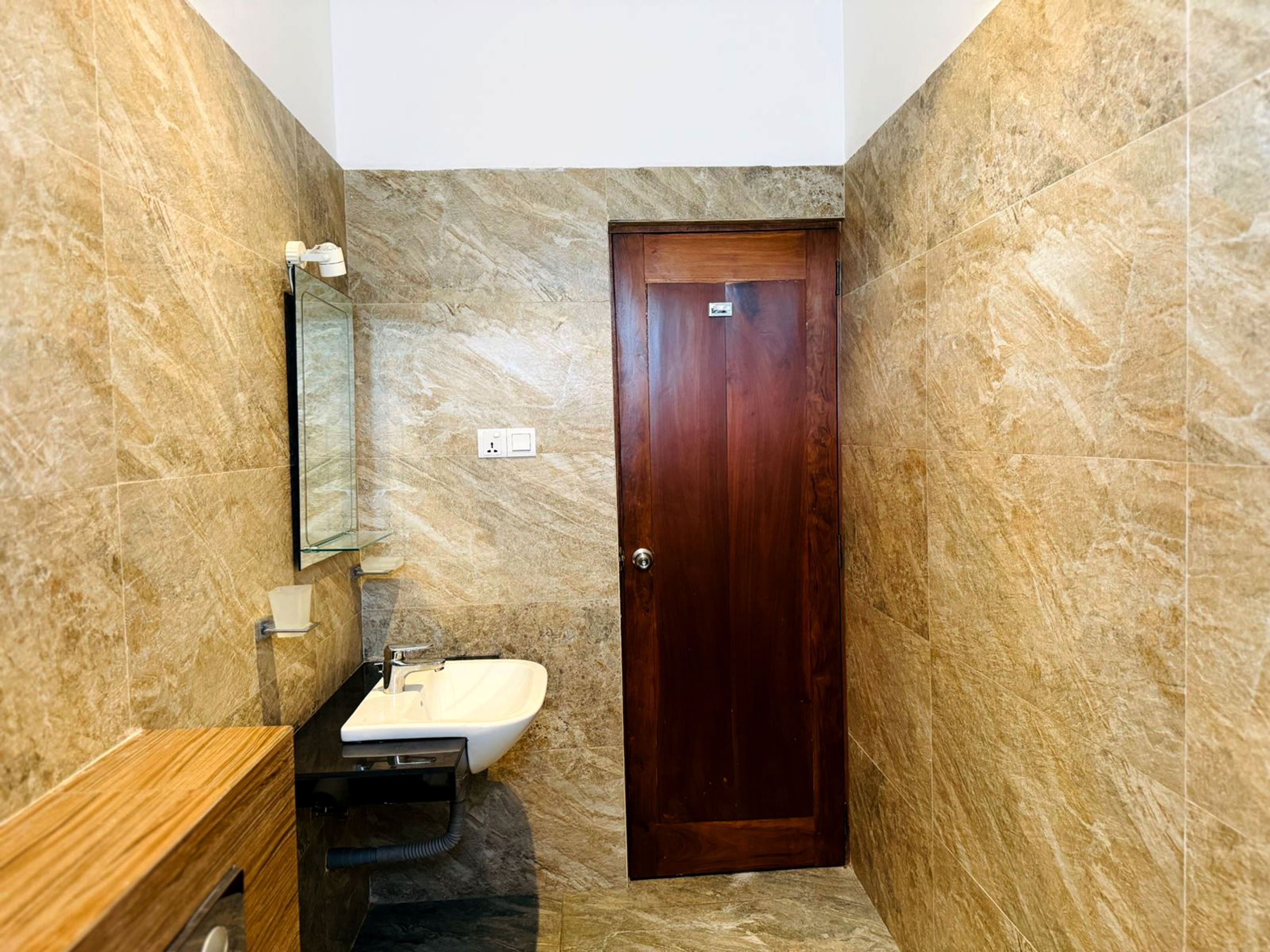 A bathroom with a marble wall, a wooden door, a sink, and a mirror.