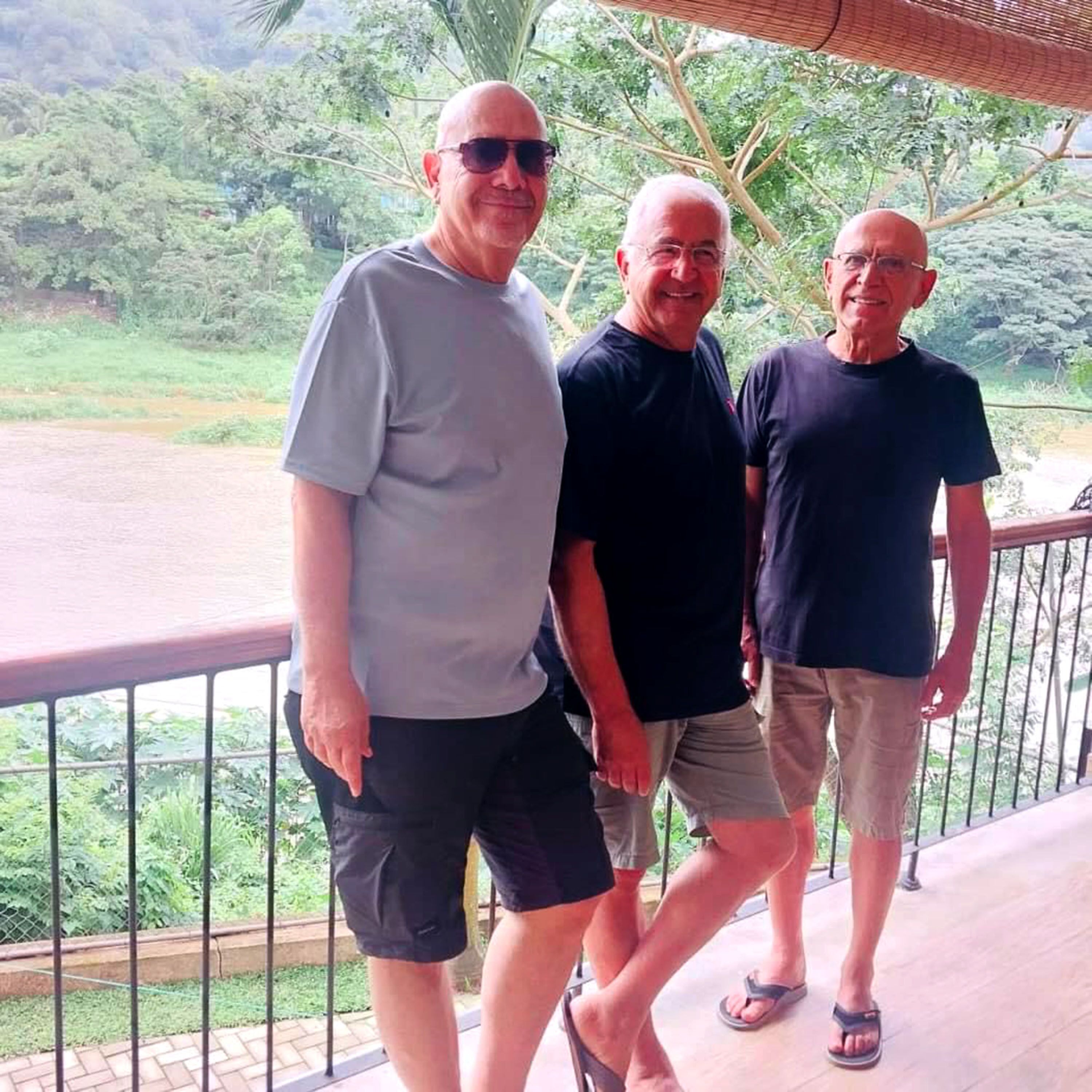 Three men standing on a balcony with a view of a lush landscape.