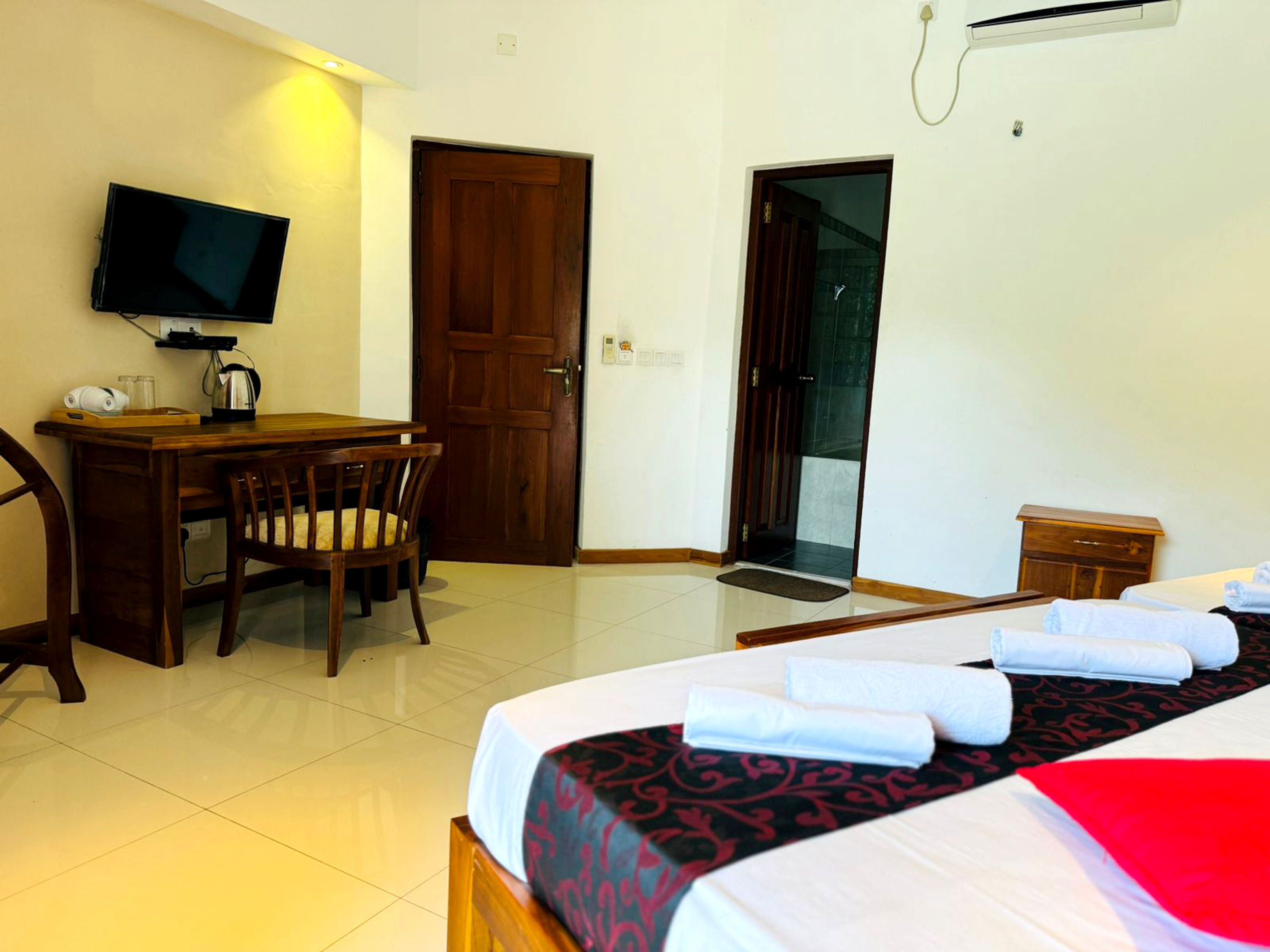 A hotel room with a bed, a desk, a chair, a television, and a door leading to a balcony.