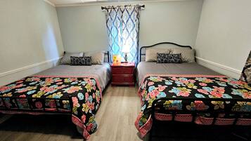 A bedroom with two beds, a nightstand, a lamp, and a window with curtains.