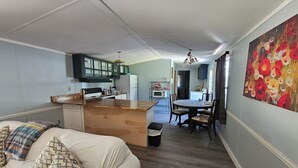 Eine kompakte Küche mit Kochinsel, ein Essbereich mit Tisch und Stühlen sowie ein Schlafzimmer mit Bett und Kissen.