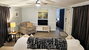 Ein Schlafzimmer mit Bett, Sessel, Fernseher, Deckenventilator und einem Gemälde an der Wand.