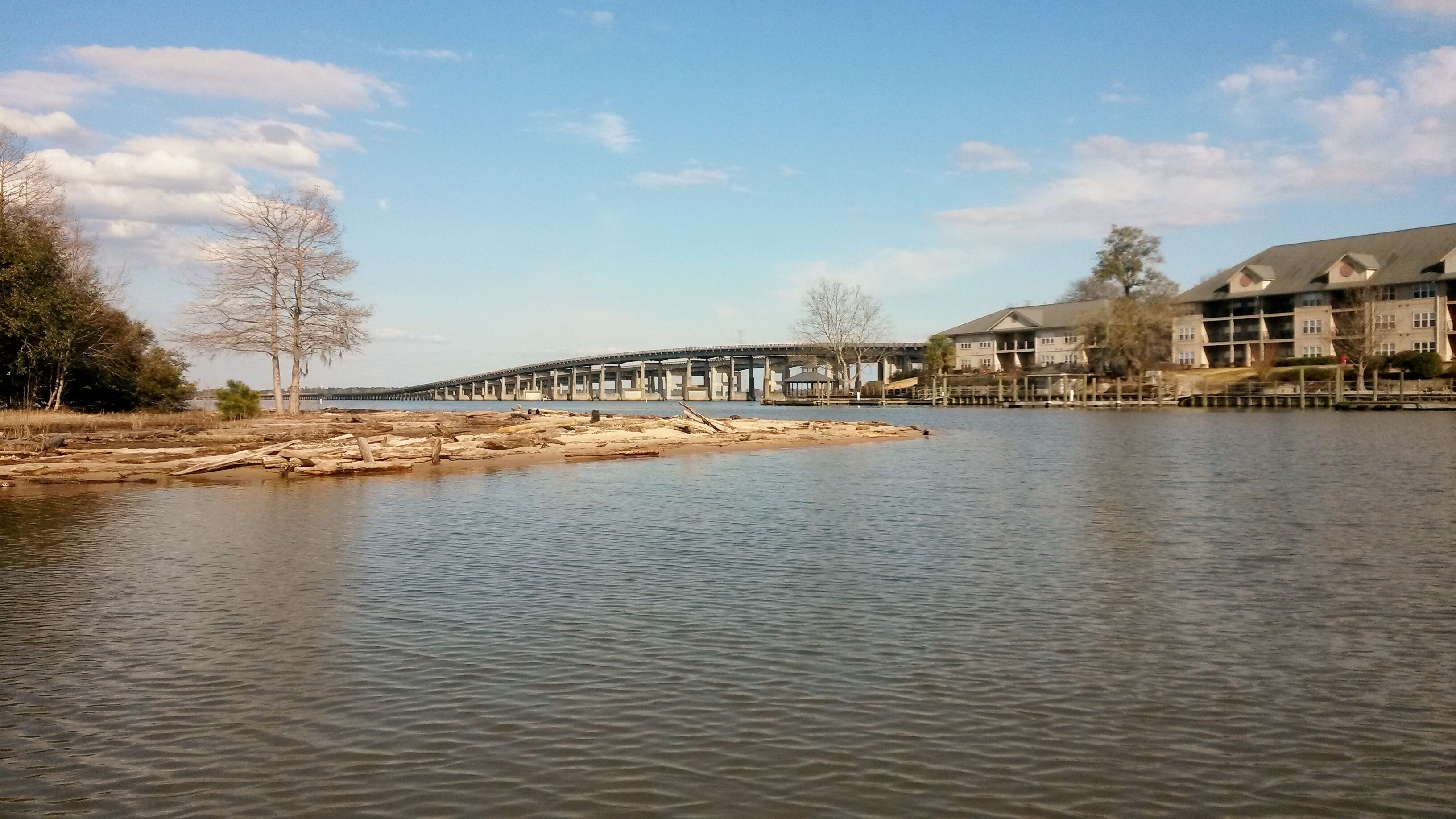 A riverside view with a bridge, trees, and a building with a balcony.