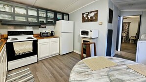 Eine kleine Küche mit Herd, Mikrowelle und Kühlschrank. Es gibt einen kleinen Essbereich mit Tisch und Stühlen.