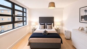 A modern bedroom with a large bed, two bedside lamps, a heater, and a view of the outside.
