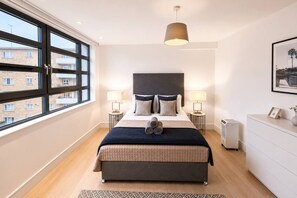 Ein modernes Schlafzimmer mit einem großen Bett, zwei Nachttischlampen, einem Heizgerät und Blick ins Freie.