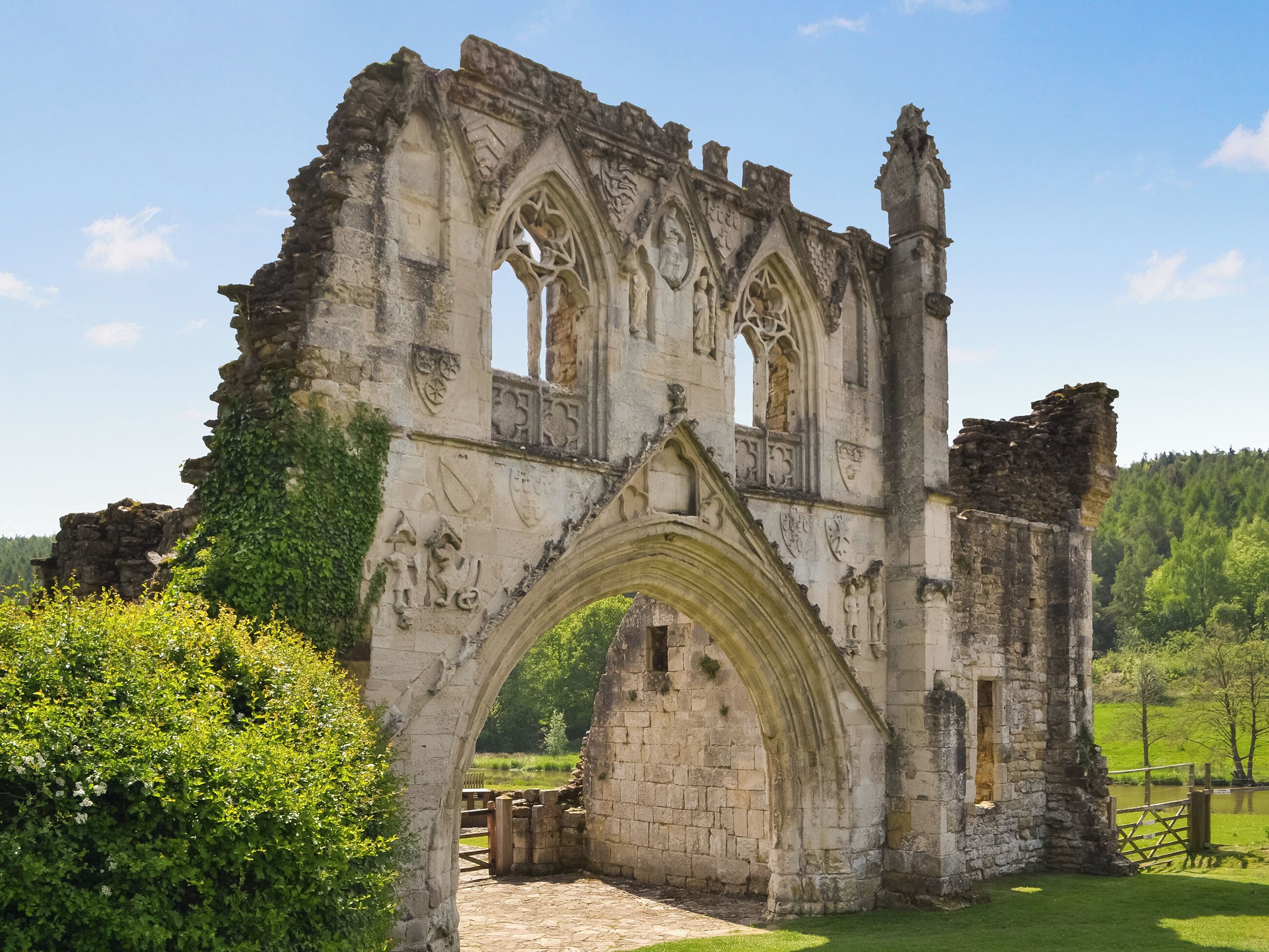 A historic stone archway with intricate carvings, surrounded by lush greenery and a clear sky.