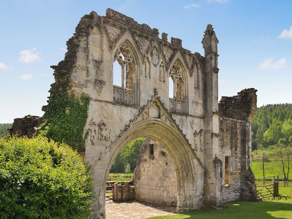 A historic stone archway with intricate carvings, surrounded by lush greenery and a clear sky.