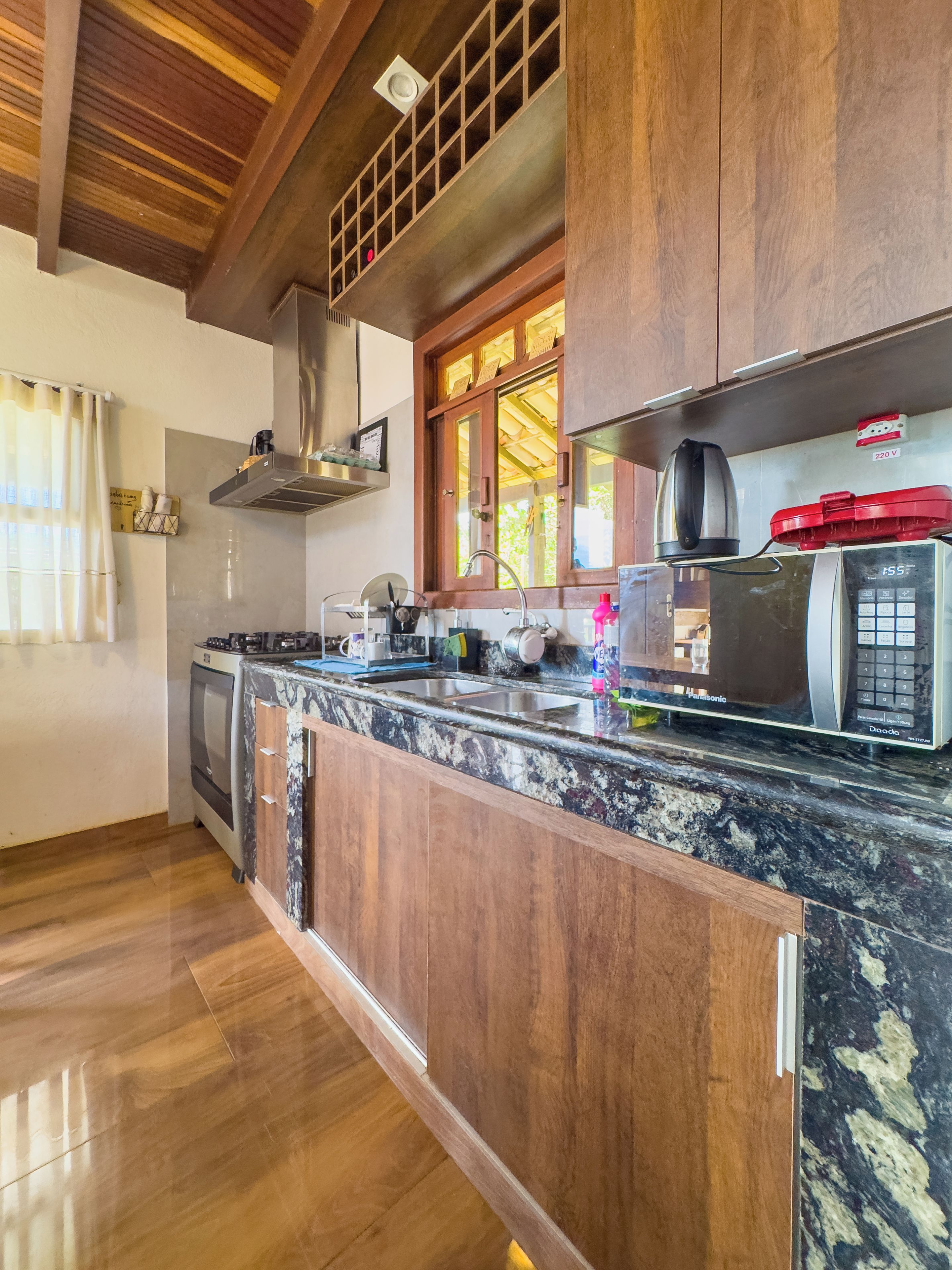 Una cocina con armarios de madera, un lavamanos de acero inoxidable, un horno empotrado y un microondas.