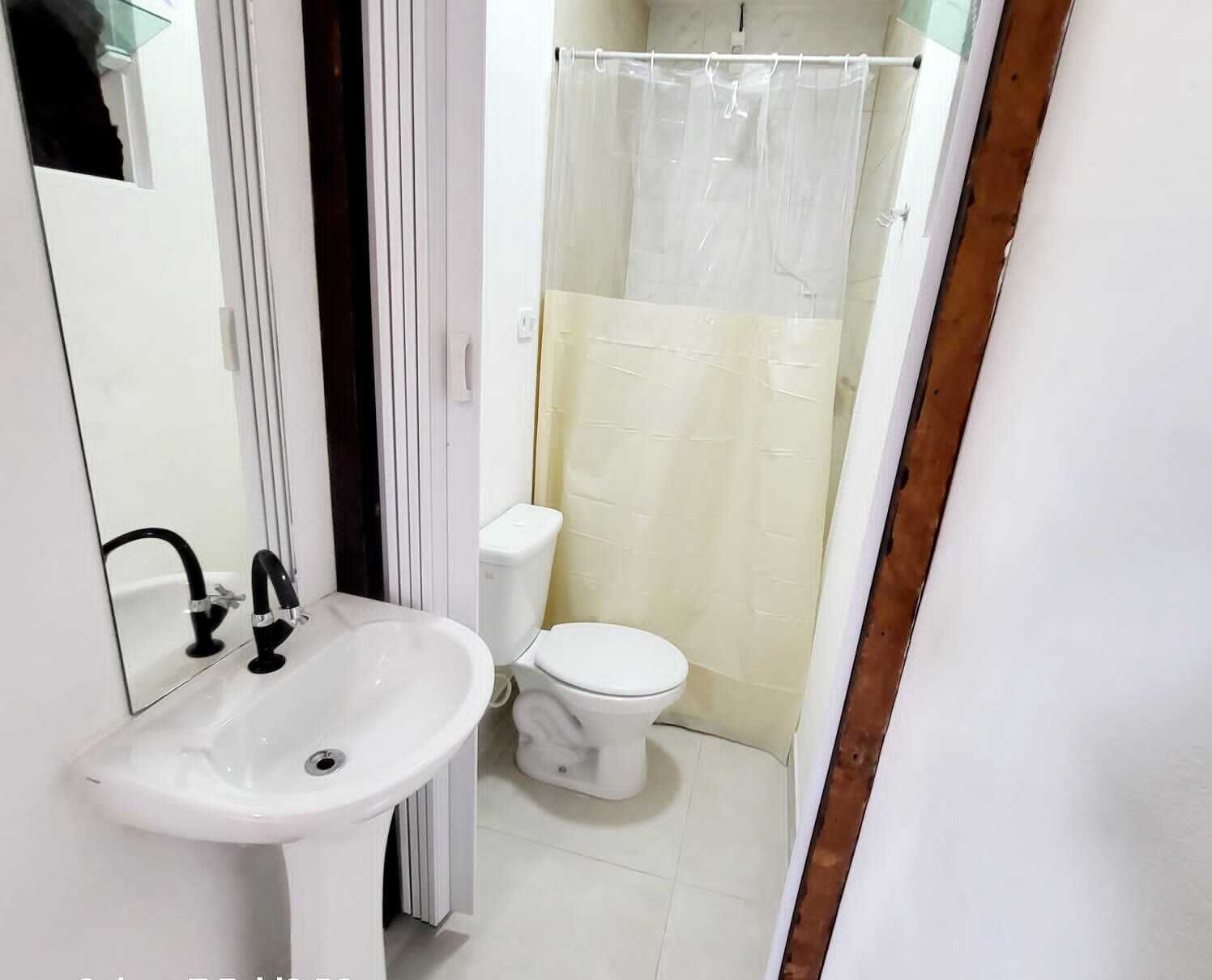 A bathroom with a white sink, black faucet, white toilet, and a shower with a transparent curtain.