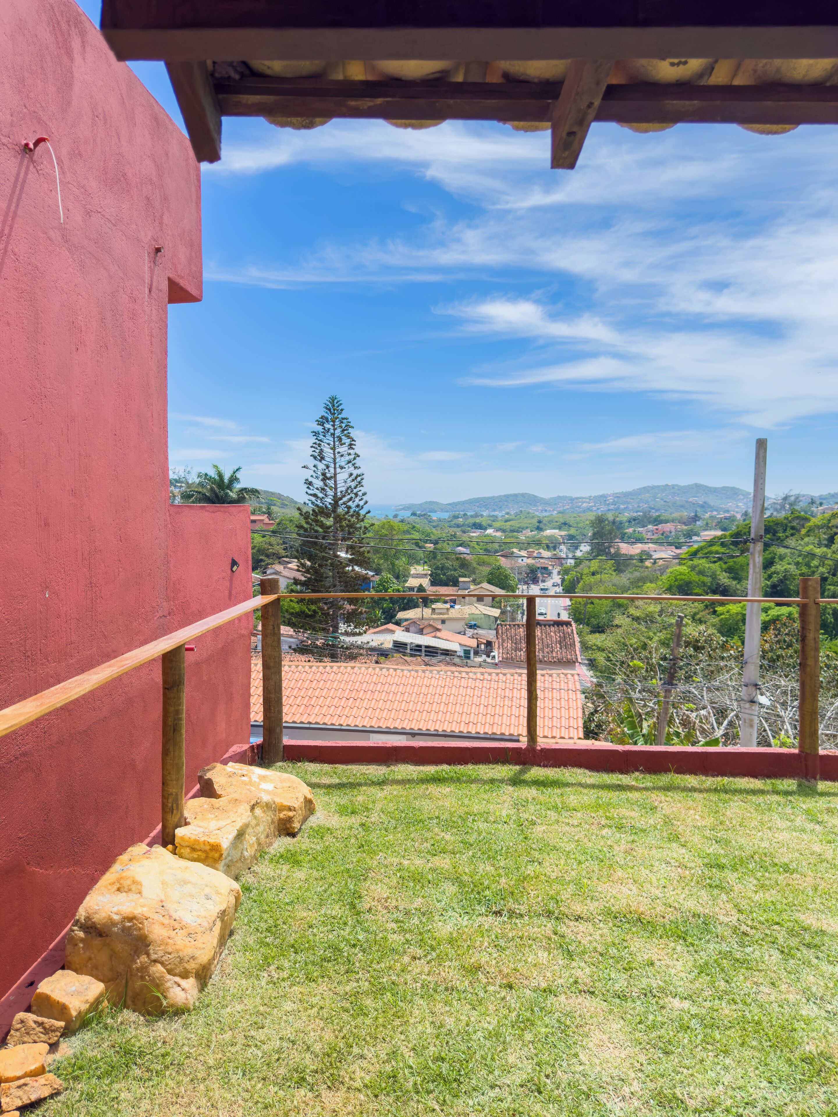 Um edifício vermelho com uma escadaria de pedra que leva a uma varanda com vista para uma cidade com casas de telhado vermelho e colinas verdes.