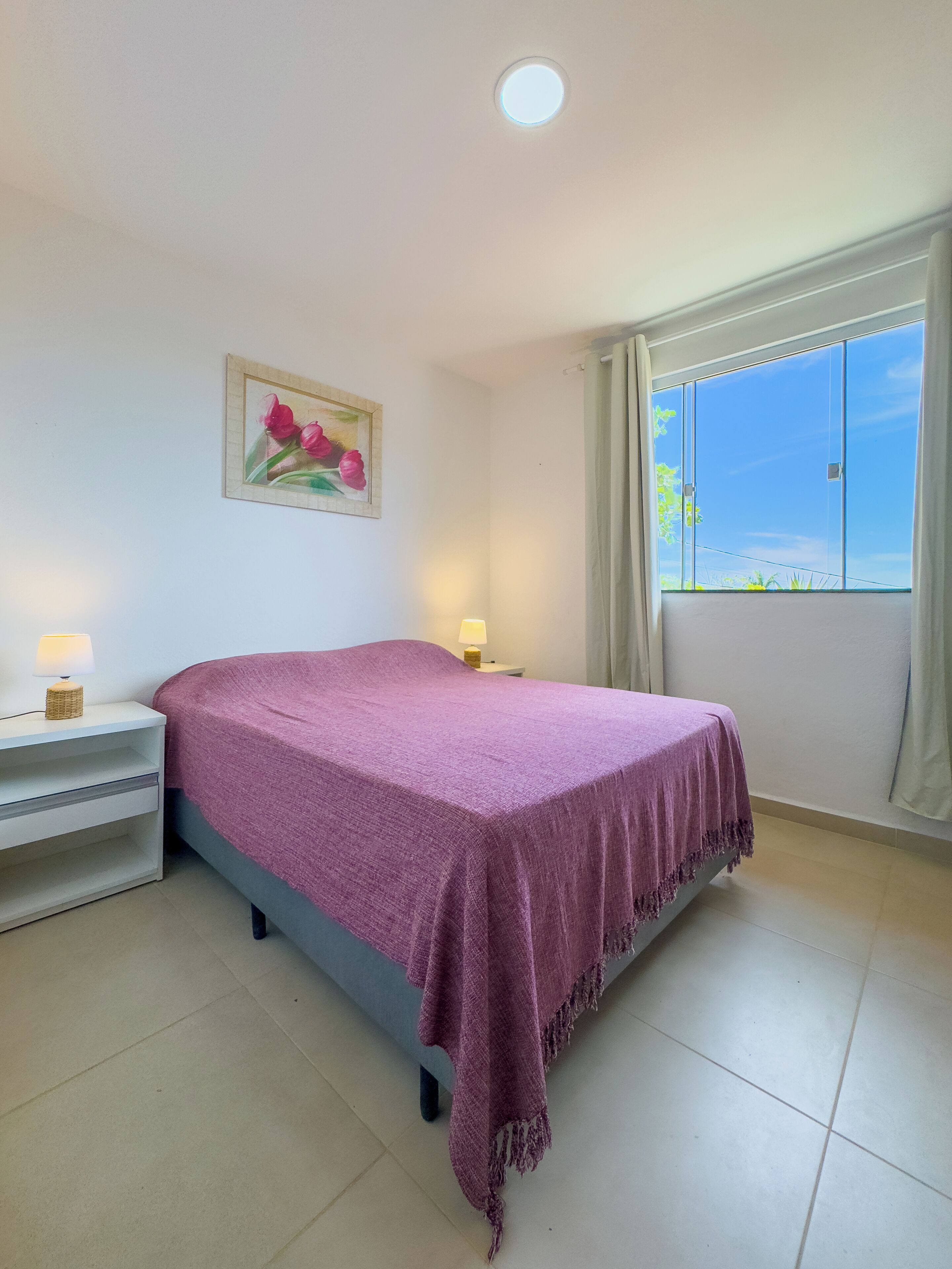 Quarto com cama, mesas de cabeceira, um quadro e janela com cortinas.