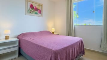 Quarto com cama, mesas de cabeceira, um quadro e janela com cortinas.