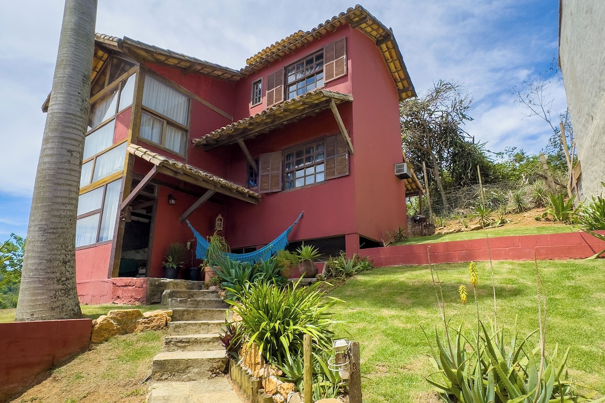 A two-story house with a red exterior, a hammock, and a stone pathway leading to the entrance.